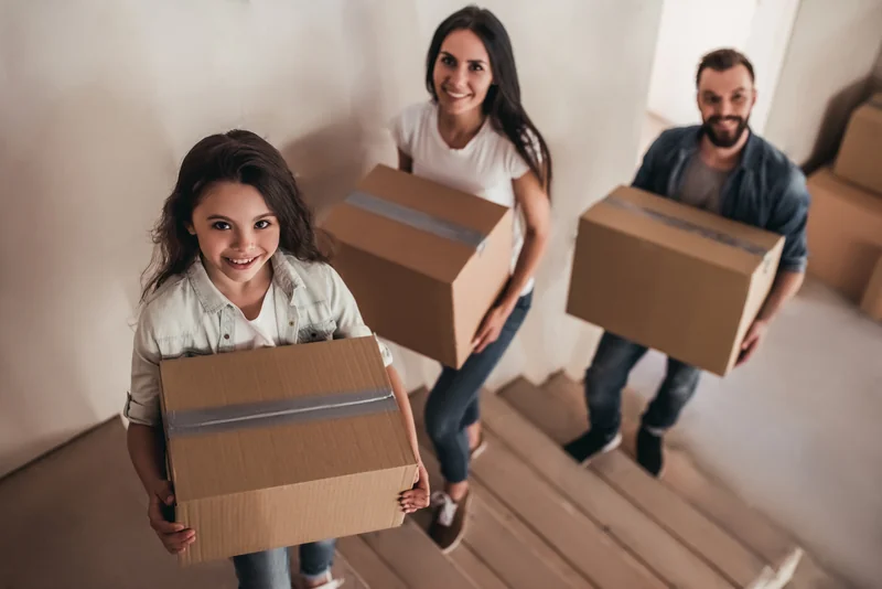 Family carrying cardboard moving boxes into their new home